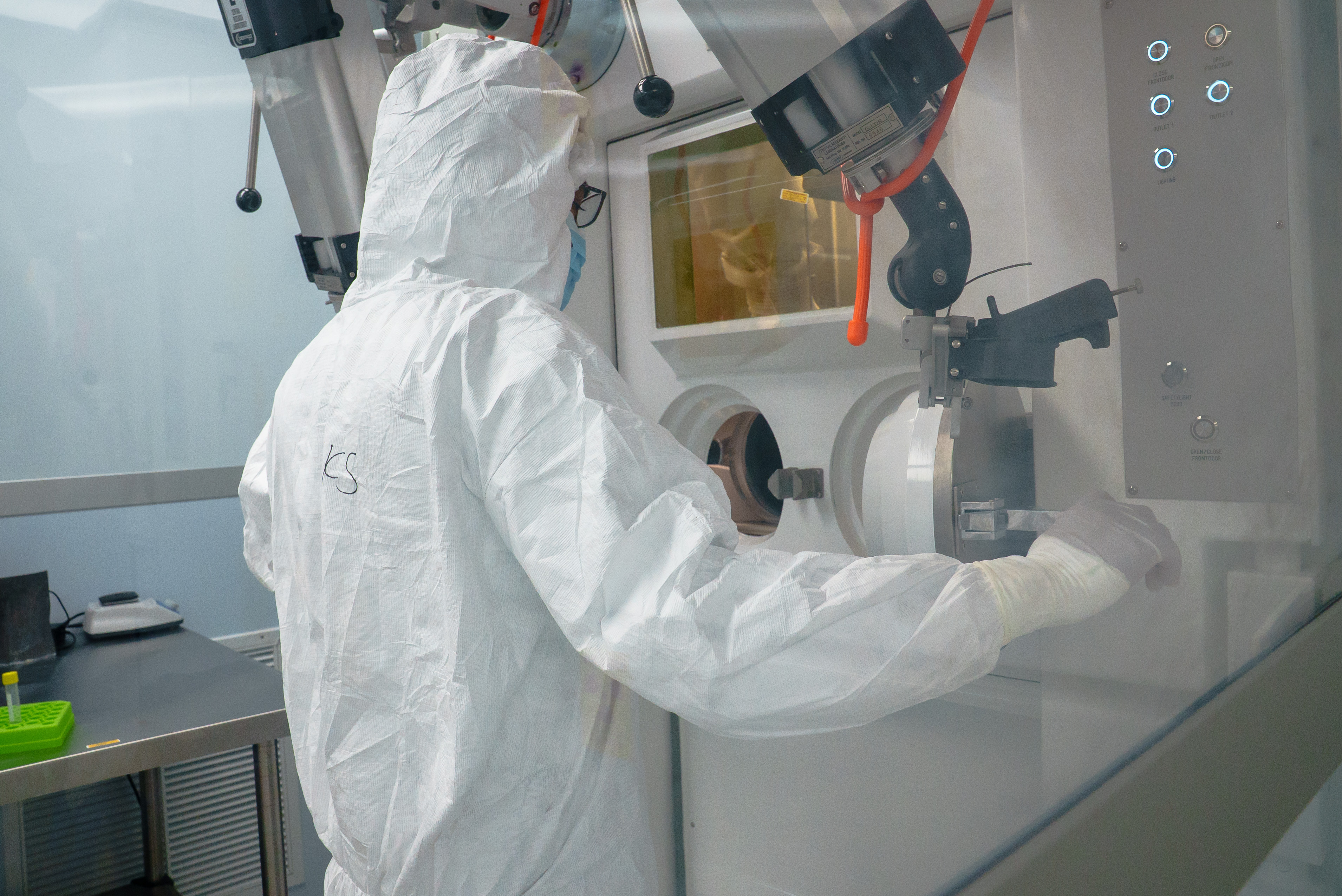 Person in a protective suit working at a sealed chamber in a laboratory