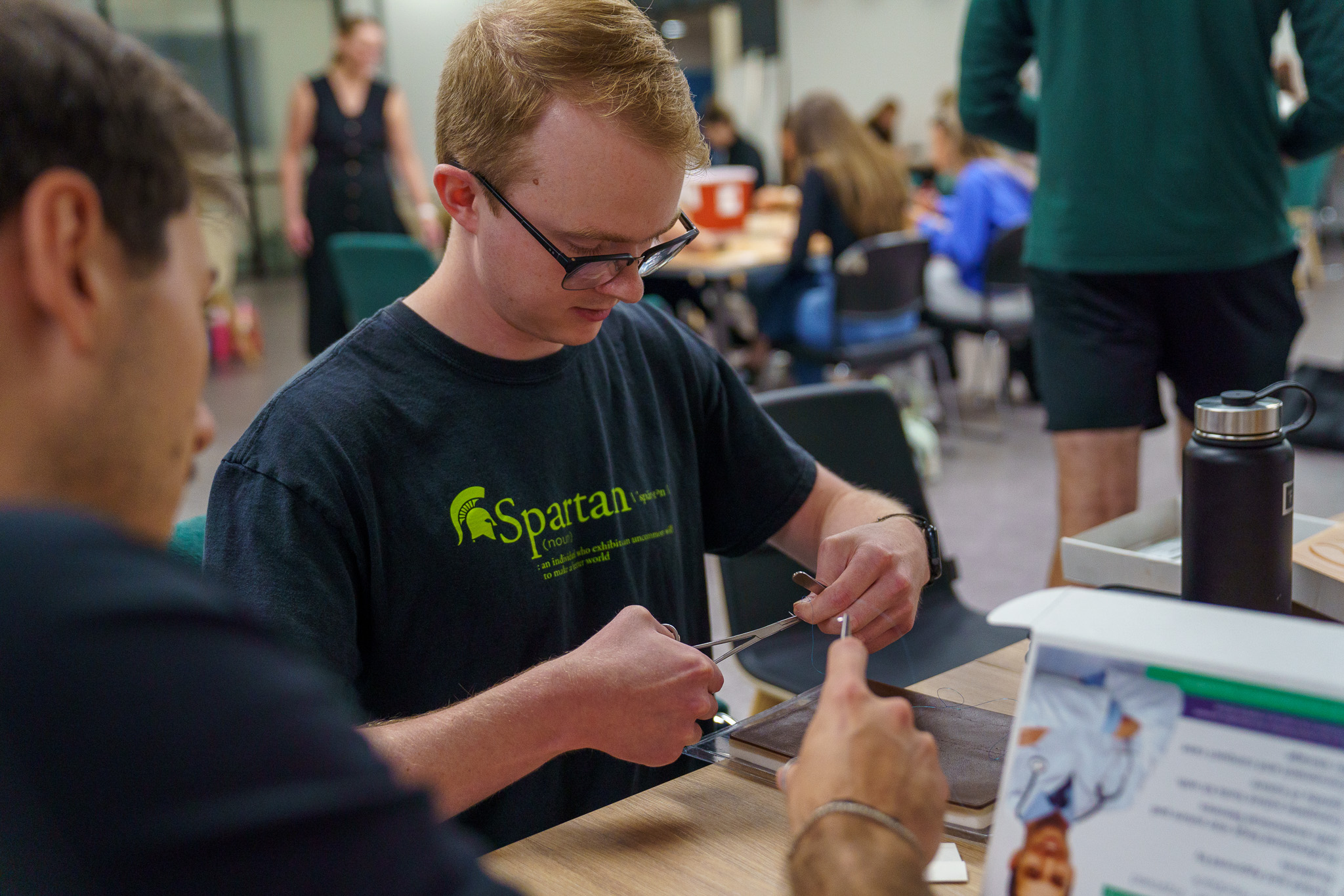 MSU College of Osteopathic Medicine PA first-year student practicing suturing on a skin tray model seated at a table