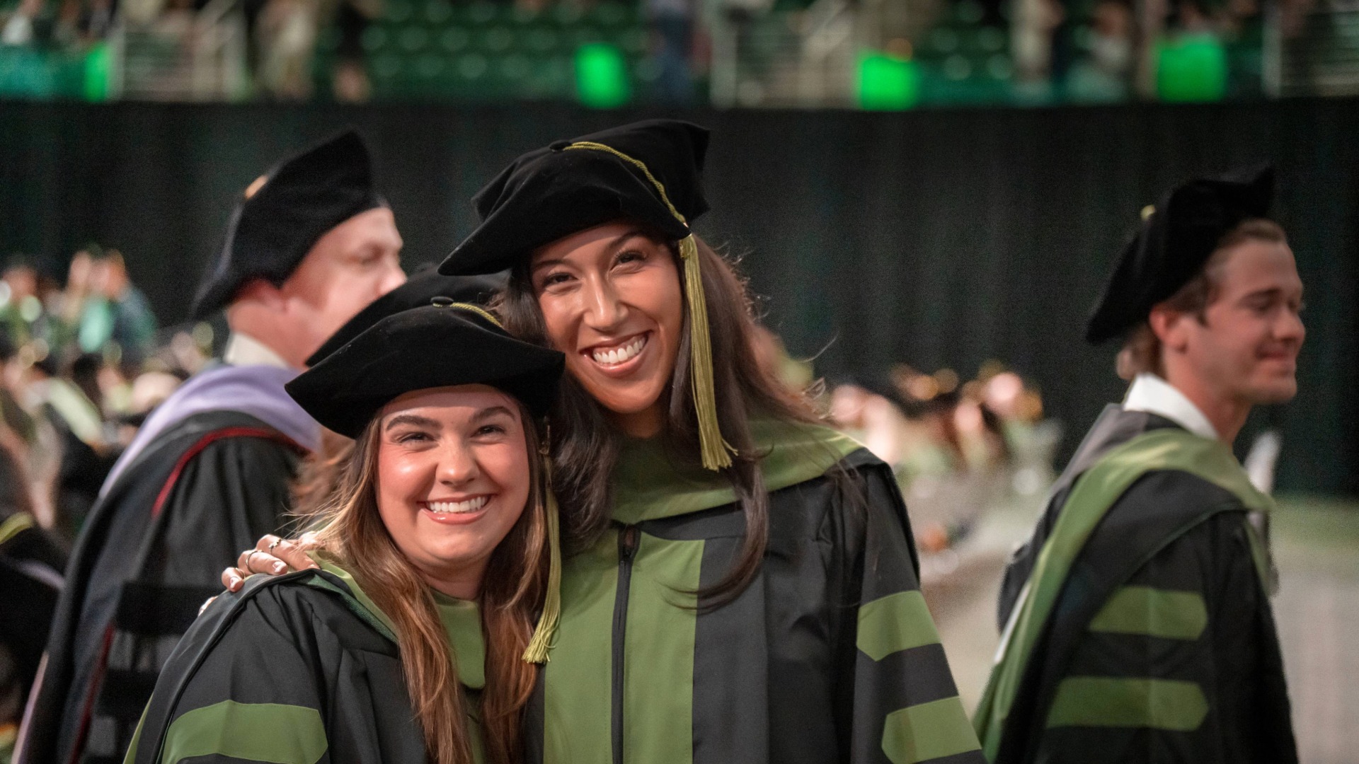 Two students giving a side hug and smiling at the camera in graduation doctoral gowns