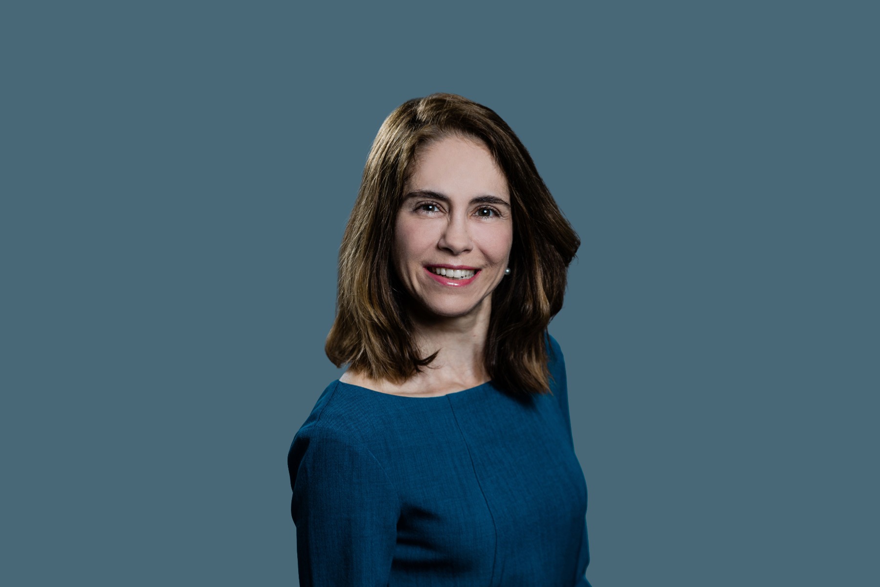 Headshot of Carolina Restini wearing a blue dress smiling with a lighter blue background.