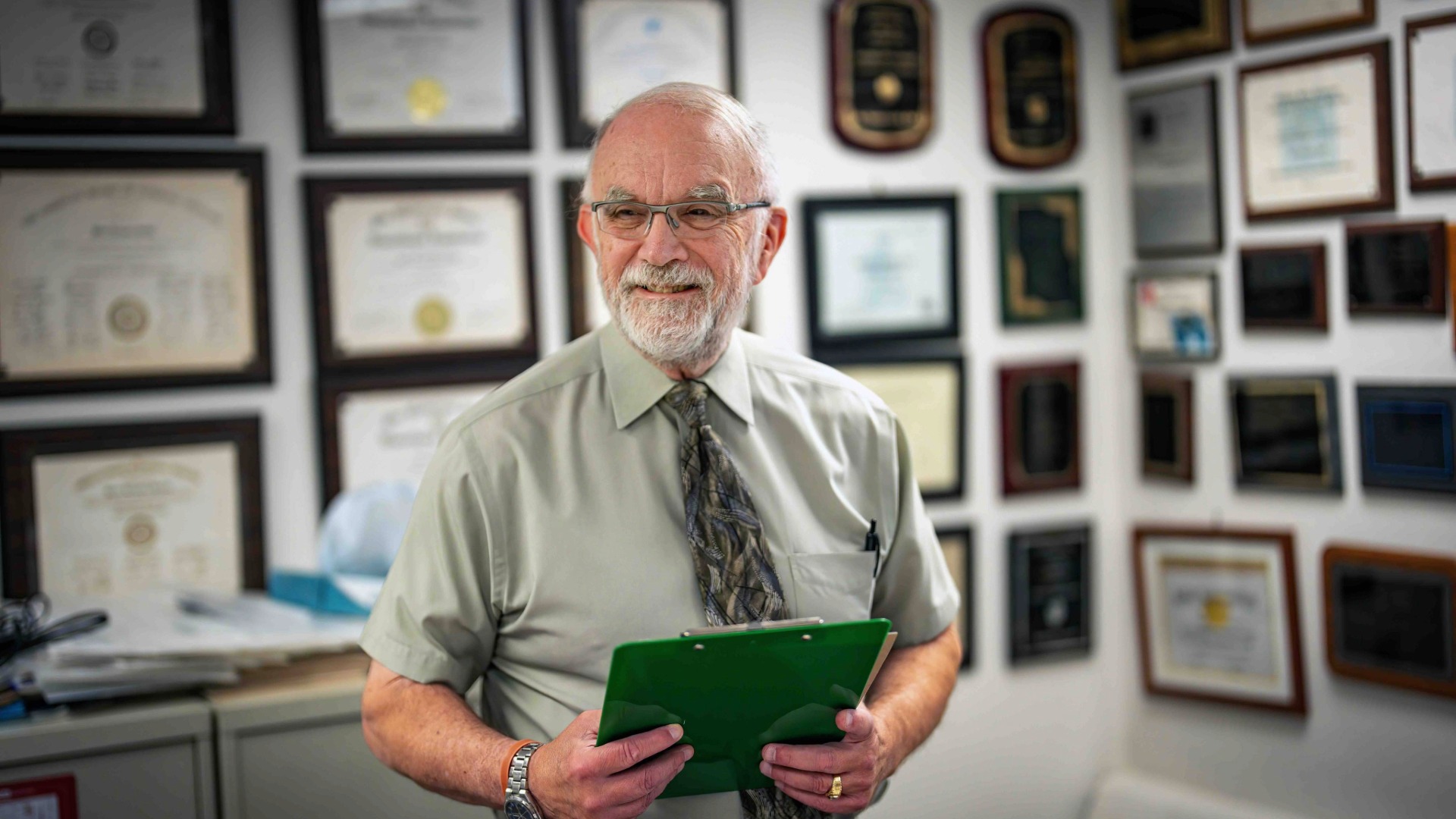 Photo of Peter Gulick looks off to the side of the camera smiling holding a green clipboard
