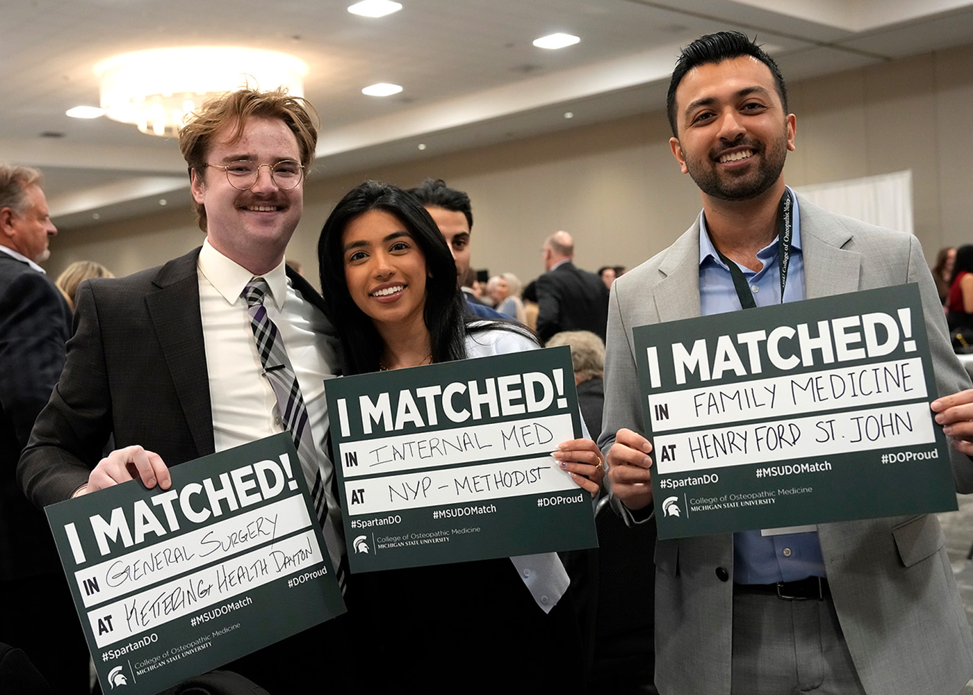 Three MSUCOM students hold signs with their Match results written on the signs