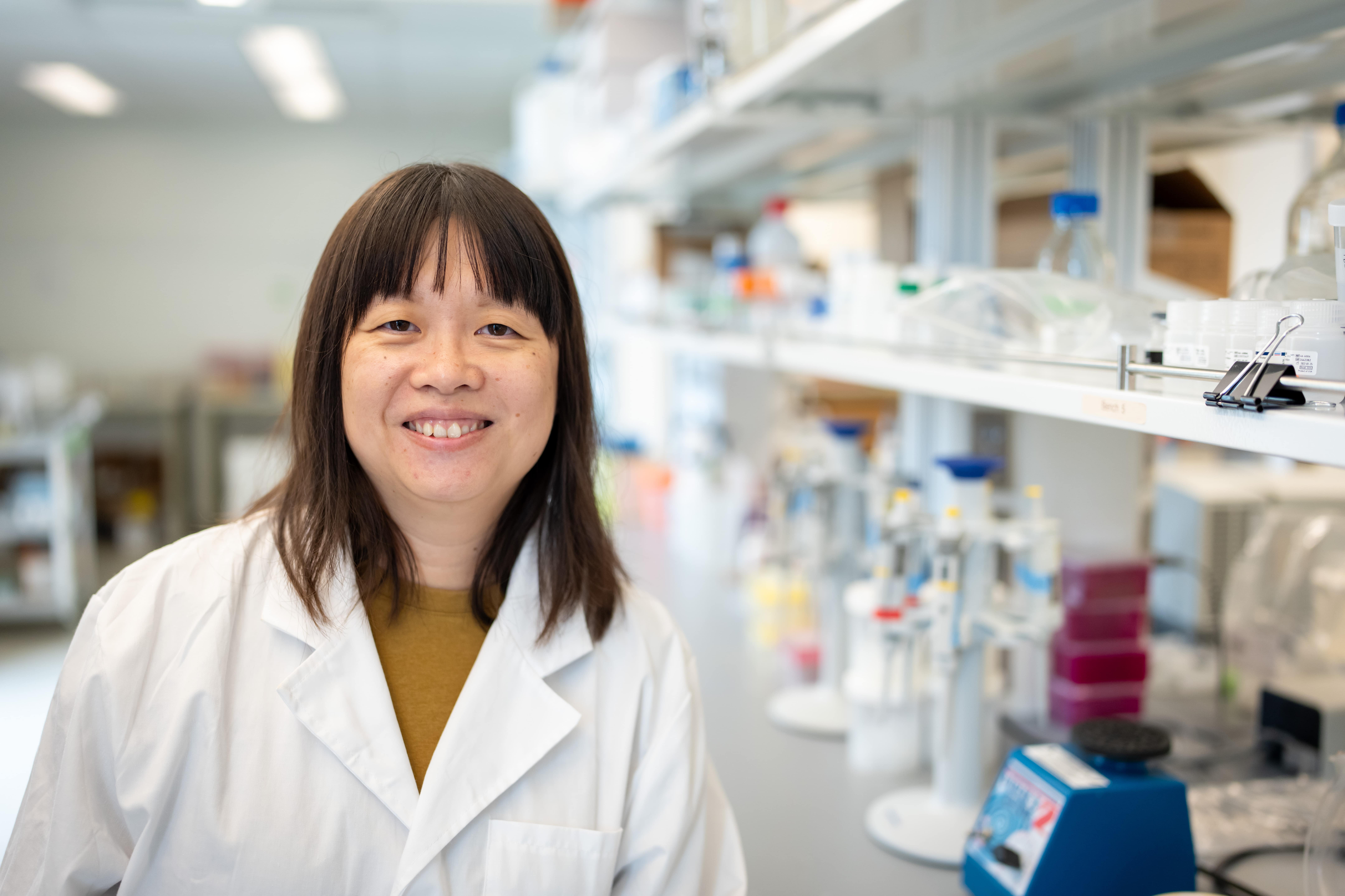 Dr. Yun Liang smiling in a lab with shelves of equipment in the background.