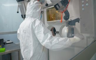 Person in a protective suit working at a sealed chamber in a laboratory