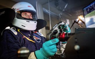 Person in a racing helmet with a steering wheel in a driving simulator.