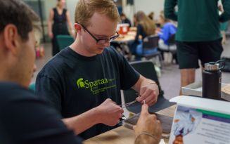 MSU College of Osteopathic Medicine PA first-year student practicing suturing on a skin tray model seated at a table