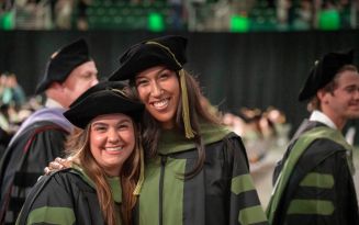 Two students giving a side hug and smiling at the camera in graduation doctoral gowns