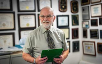 Photo of Peter Gulick looks off to the side of the camera smiling holding a green clipboard