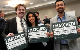 Three MSUCOM students hold signs with their Match results written on the signs