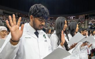 Students raising their right hand holding a paper reciting the osteopathic oath during the white coat convocation ceremony
