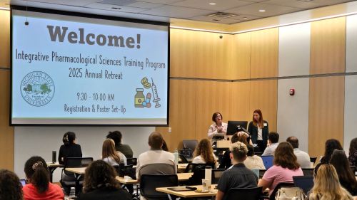 Classroom lecture filled with people seated facing away towards a lecture slide projected saying Welcome! Biological Sciences Training Program Annual Retreat.