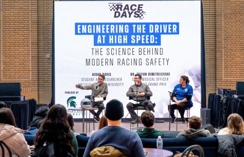 Three speakers on stage at an event discussing racing safety with an audience in attendance