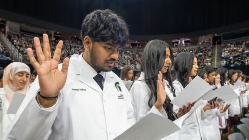 Students raising their right hand holding a paper reciting the osteopathic oath during the white coat convocation ceremony